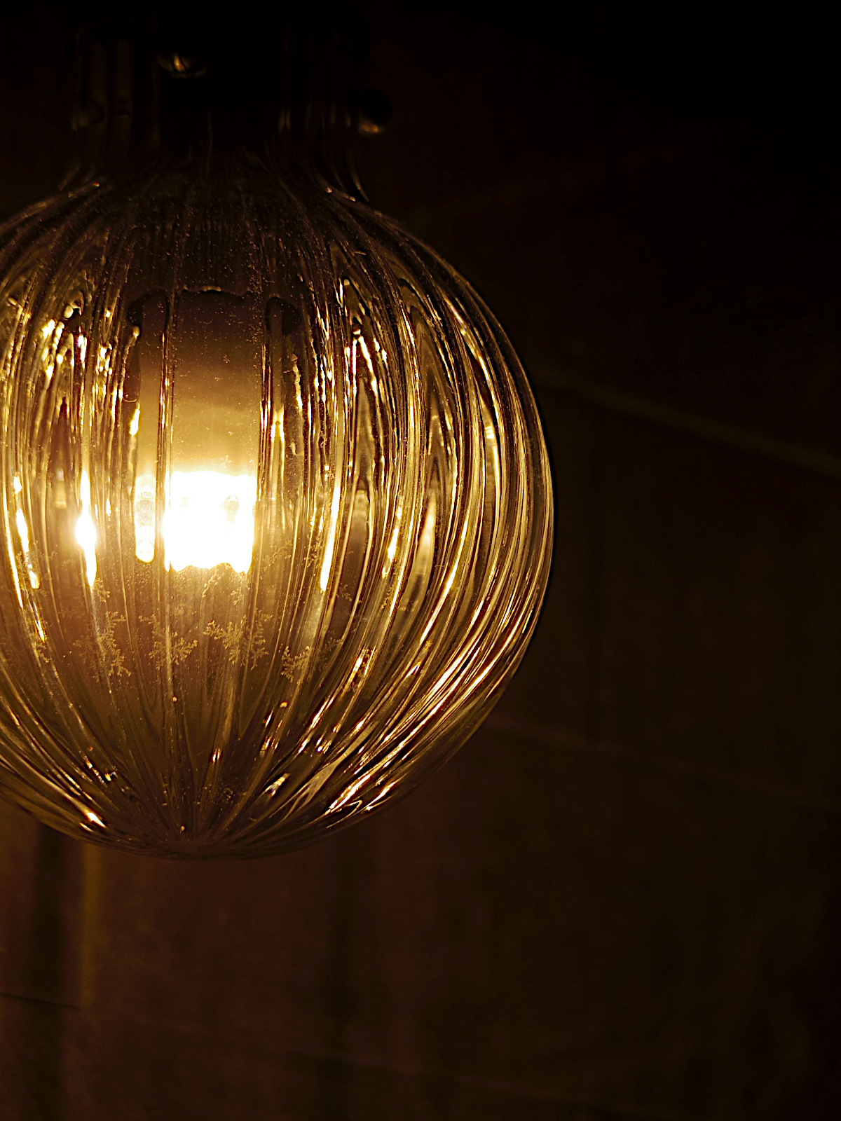 気泡入りガラスシェードが温かみのある灯りを放つトイレ照明。ブラックトーンの内装と調和した上質なリフォーム空間。