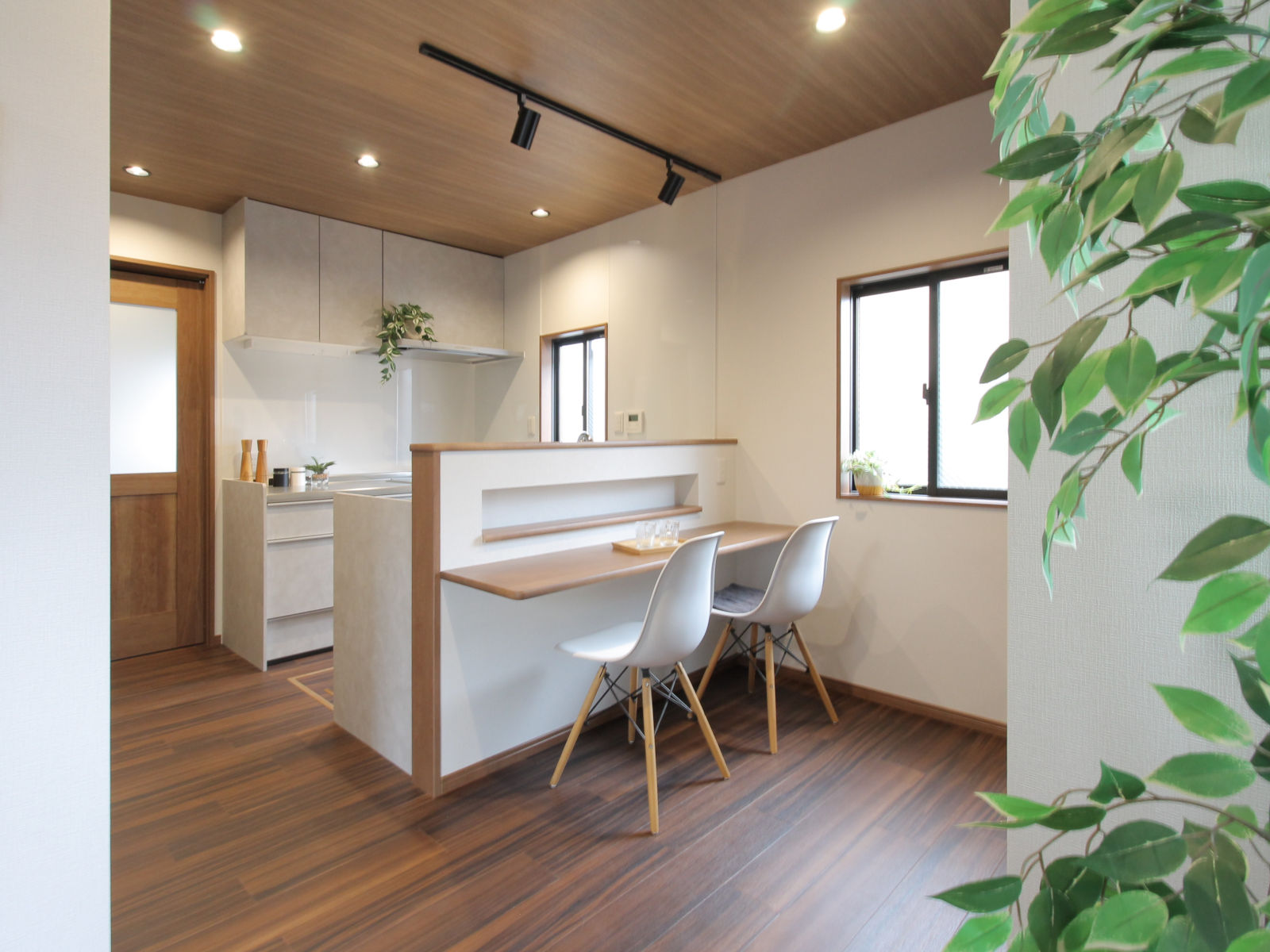 木目調の天井SP9805にダウンライトとスポットライトを組み合わせ、LIXILシエラSの並列型対面キッチンと造作カウンターを柔らかく照らす。