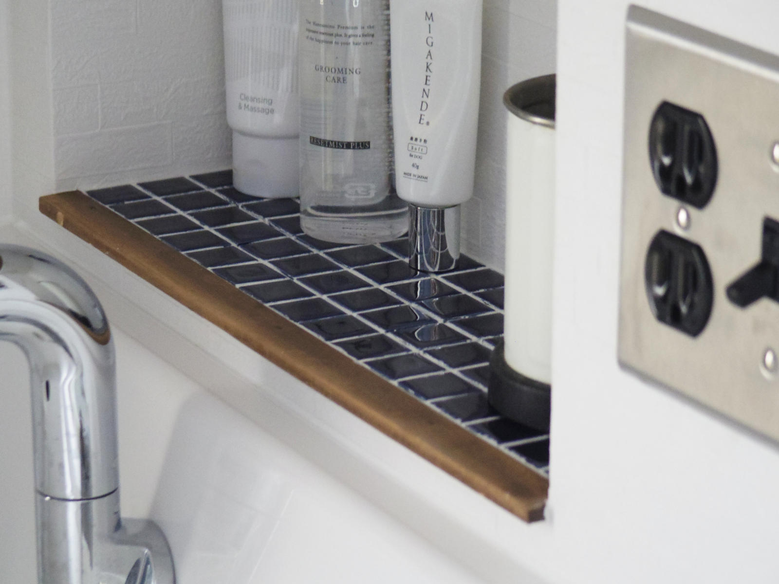 ミラー下に造作したニッチ棚にはネイビーのモザイクタイルを採用。スキンケア用品をすっきり収納でき、木縁仕上げがアクセントに。