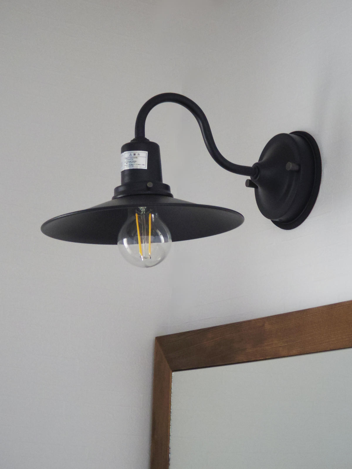 黒のマットなブラケットライトが空間を引き締め、木枠ミラーとのコーディネートが映える。インダストリアルとナチュラルを融合した洗面事例。