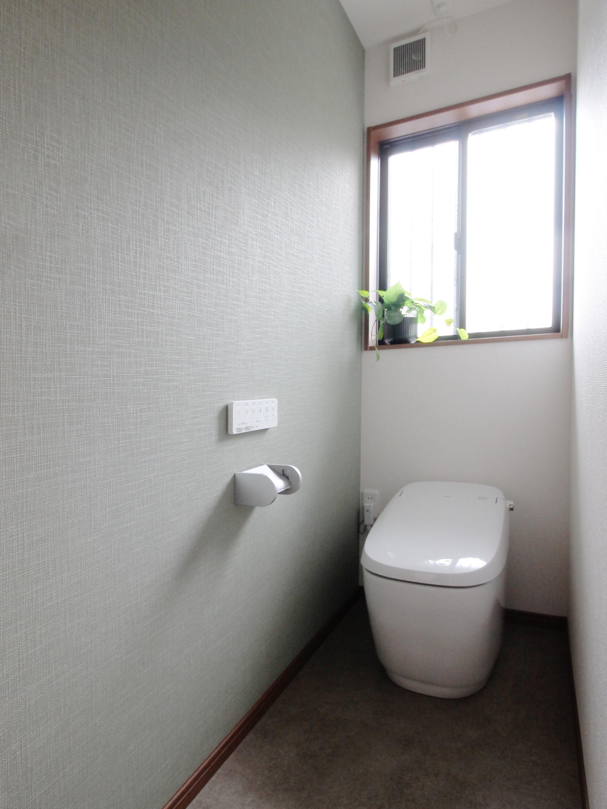 グリーンのアクセントクロスを取り入れた、LIXILサティスGを採用したトイレ。サンゲツのIS-2025とRE-55155の組み合わせ。名古屋の戸建てリノベーションで快適さとデザインを両立。