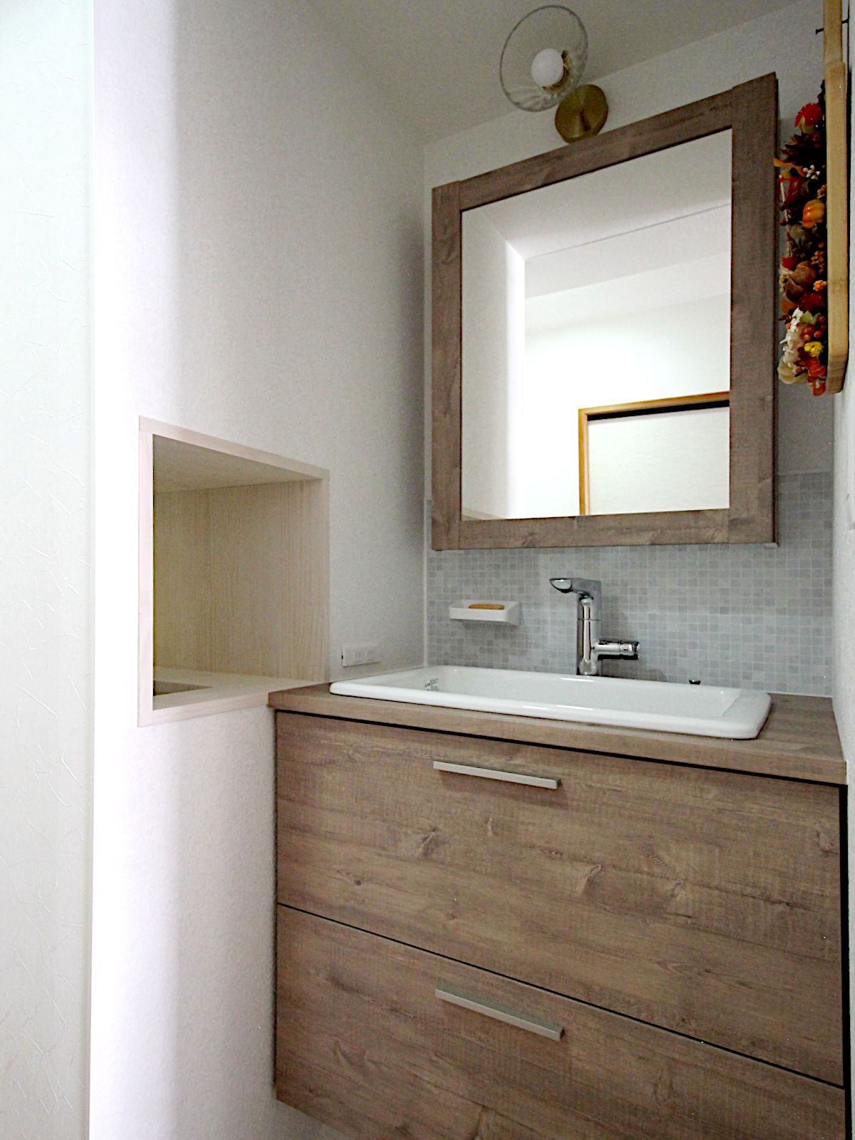 マンションリノベーション事例。洗面化粧台ドレーナとランドリールームをつなぐ小窓を設け、タオルの受け渡しができる便利な動線設計。ホワイト系クロス【FE-1164】で清潔感ある印象に。