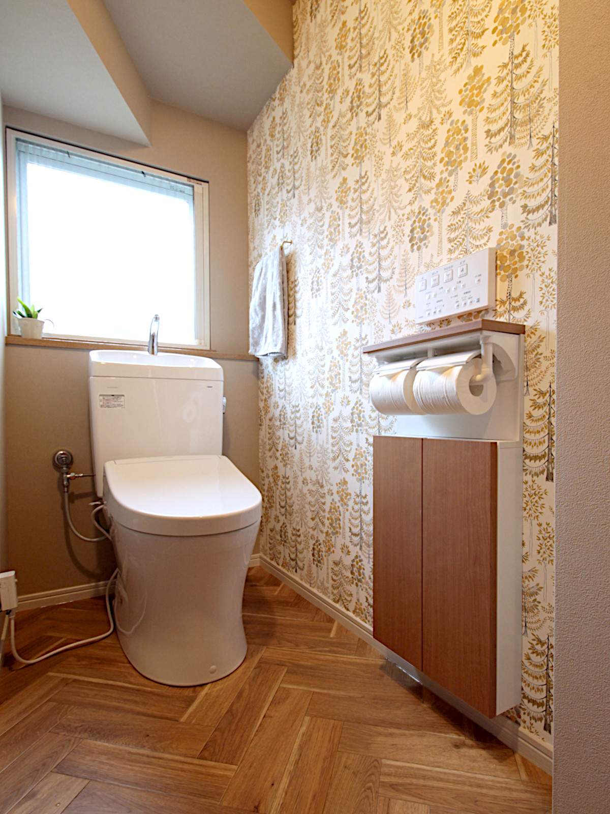 北名古屋市のトイレリフォーム。サンゲツ【HM-12090】【RE55775】【RE55038】を使用し、ツリー柄アクセントクロスと木目収納【LIXIL TSF-221U クリエモカ色】で北欧カントリー調に仕上げた空間。