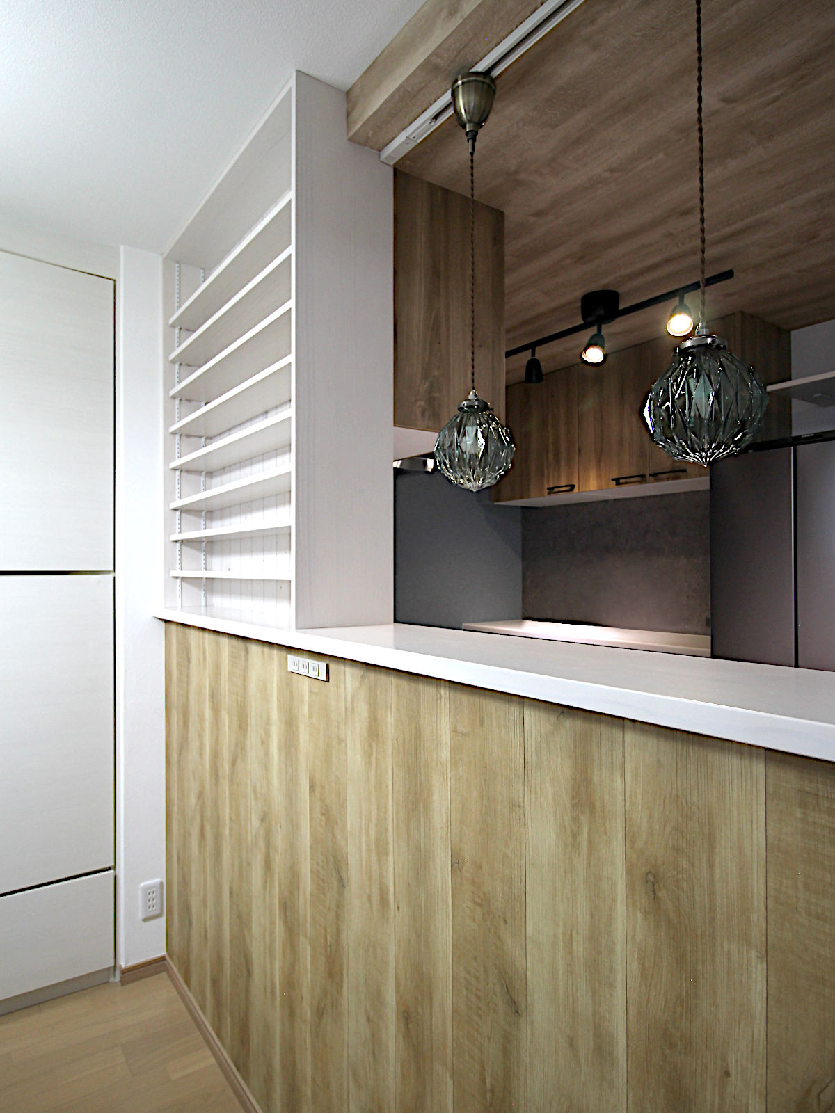 マンションリノベーション事例。ペンダントライトが印象的な対面キッチン。木目腰壁と白カウンターがやさしく調和するデザイン。