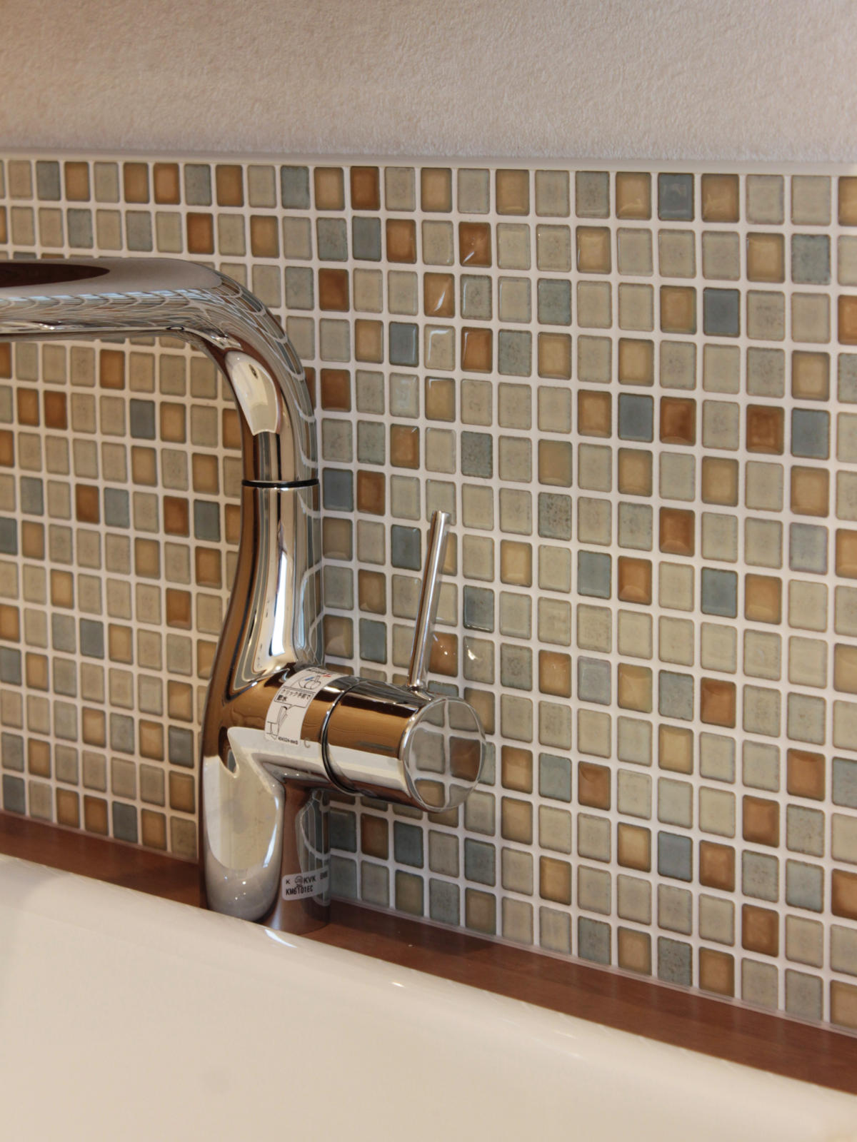 LIXILスマートモザイクシートSMTS-630/KLG-11を採用。ベージュやグレーのやさしい色合いが木製カウンターと調和し、洗面所を温かく彩る。