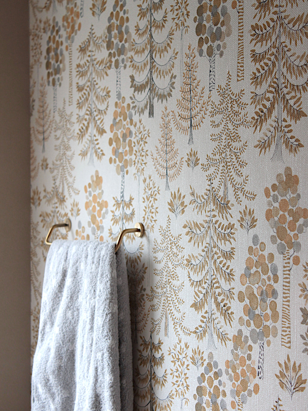 北名古屋市のトイレリフォーム事例。サンゲツ【RE55775】のツリー柄クロスを採用し、金とグレーの樹木が浮かぶ北欧デザイン。柔らかな質感が特徴。