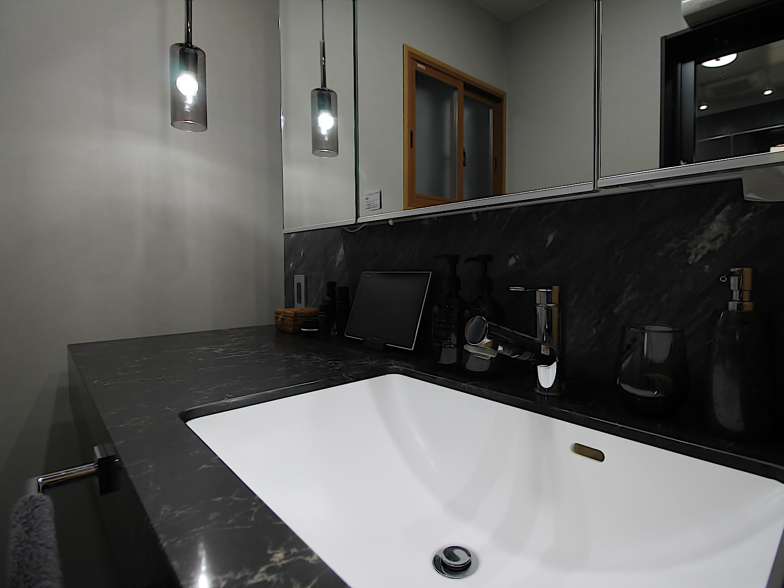 洗面リノベーション事例。グレートーンの内装とペンダントライトの組み合わせで上質な陰影を演出。サンゲツ【RE-53189】採用。