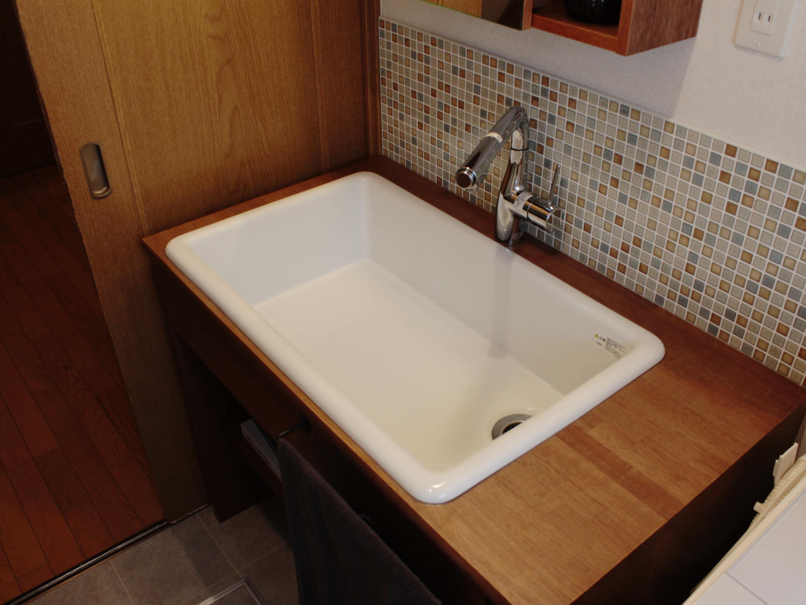 北名古屋市のリノベーション事例。TOTO病院用シンクを採用した造作洗面台。底が平らで愛犬の足洗いやシャンプーも安定。木製カウンターとタイル壁【LIXIL スマートモザイクシートSMTS-630/KLG-11】でナチュラルな雰囲気に。